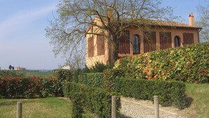 A rustic building with a sloped roof, surrounded by well-maintained hedges and a gravel path. - Pero – Two Level Apartment in Tuscan Farmhouse with Swimming Pool, 2 Bedrooms (Castelfiorentino)