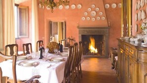 Un comedor con chimenea, sillas de madera, una mesa dispuesta para una comida y una araña.