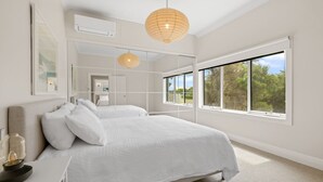 Camera da letto con un letto grande, un comodino, uno specchio e una finestra vista alberi.