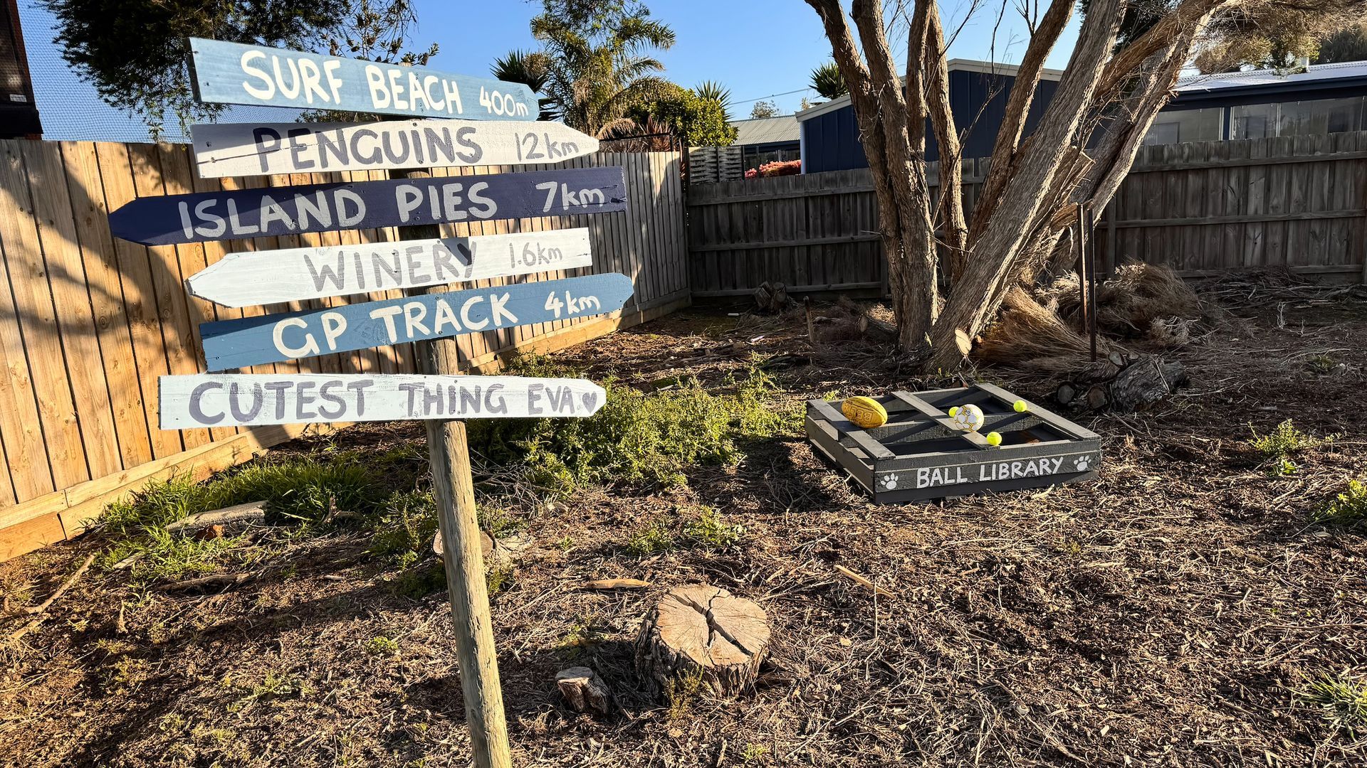 A wooden signpost with directional signs indicating distances to various local attractions such as Surf Beach, Penguins, Island Pies, Wineries, GP Track, and a Ball Library.