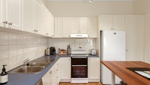 Una cucina moderna con mobili bianchi, un lavello in acciaio inossidabile, un forno integrato e un frigorifero bianco.