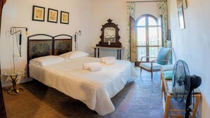 A bedroom with a large bed, a wooden ceiling, a table with a lamp, a chair, and a fan. - Plum – Two-Level Apartment in Tuscan Farmhouse with Swimming Pool, 2 Bedrooms (Castelfiorentino)