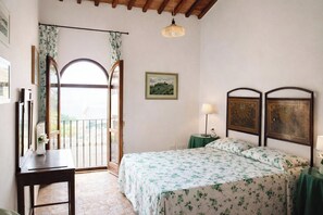 A bedroom with a bed, a desk, a chair, a nightstand, a lamp, a picture on the wall, and a balcony with curtains. - Plum – Two-Level Apartment in Tuscan Farmhouse with Swimming Pool, 2 Bedrooms (Castelfiorentino)