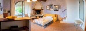 A cozy bedroom with a bed, a small table, a chair, a fireplace, and a window overlooking greenery. - Plum – Two-Level Apartment in Tuscan Farmhouse with Swimming Pool, 2 Bedrooms (Castelfiorentino)