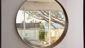 Un miroir rond accroché au mur reflète un balcon avec un canapé, une table et une vue sur des palmiers et un immeuble.