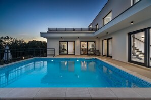 Ein modernes Haus mit Schwimmbad, großen Fenstern und einem Balkon.