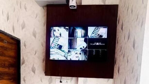 A room with a flat-screen TV mounted on the wall, a wooden door, a small trash bin, and a pink chair. - Hotel Shree Kanhaiya Palace vrindavan  (Vrindavan)