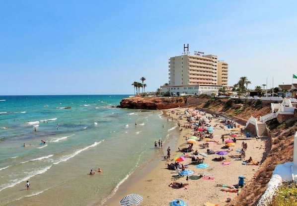 A beach with a hotel named "Hotel San Antonio La Tena" on a cliff overlooking the sea. - Stylish South House in Villamartin - Solarium and Poolview Terrace (Orihuela)