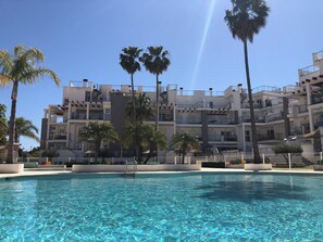 Ein modernes Hotel mit Swimmingpool, Palmen und blauem Himmel.