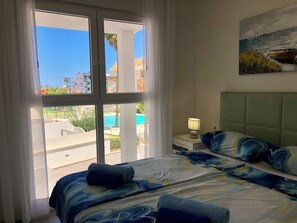 Ein Hotelzimmer mit großem Fenster, einem Bett mit blau-weißer Bettwäsche, einem Nachttisch mit Lampe und einem Bild an der Wand.