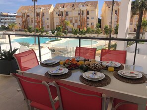 Ein Balkon mit Esstisch, gedeckt für das Frühstück, mit Blick auf einen Swimmingpool und Wohnhäuser.