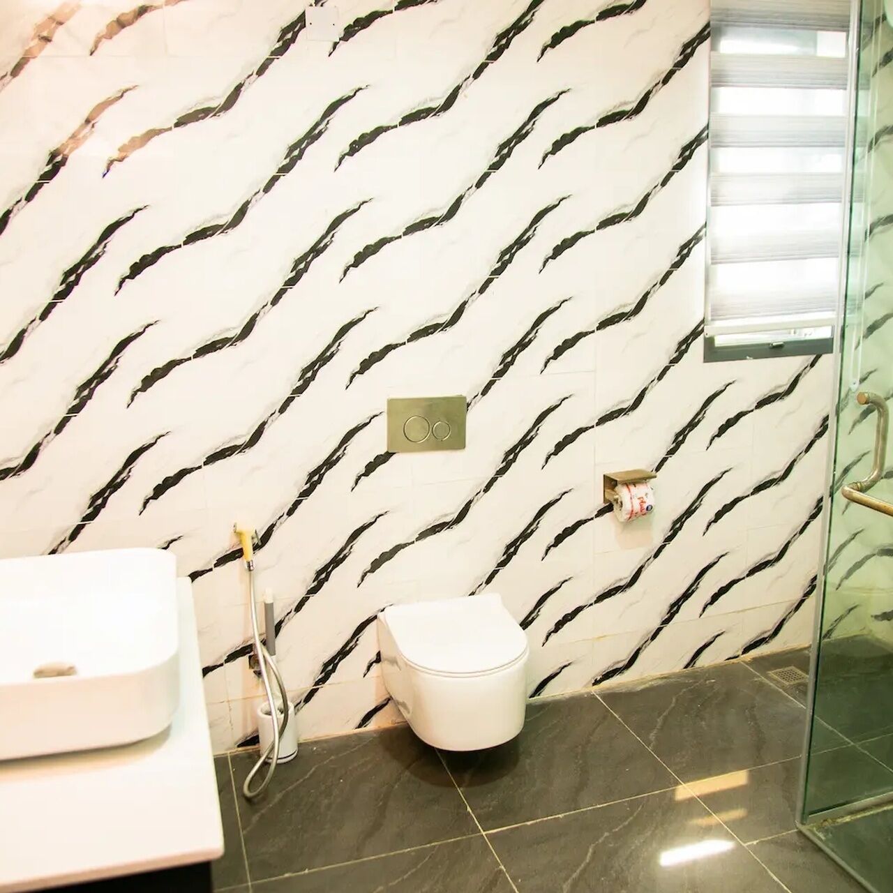 A bathroom with a marble wall, a toilet, a sink, and a glass shower enclosure.