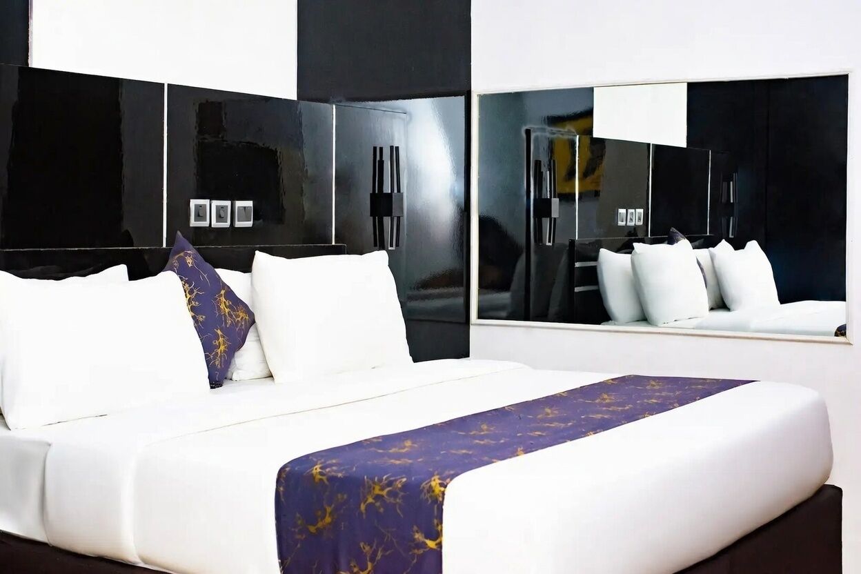 Una habitación de hotel moderna con una cama grande, una paleta de colores blanco y negro y un espejo amplio.