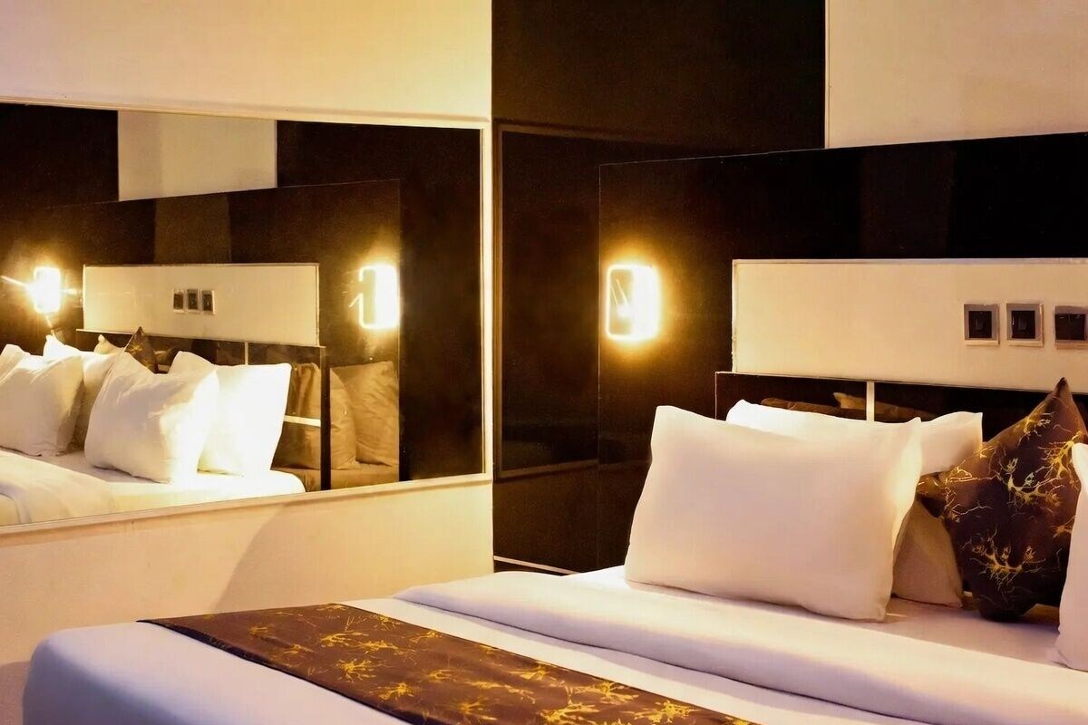 A modern hotel room with a large bed, a mirror, and wall-mounted lights.