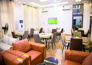 A hotel room with leather sofas, a dining area with tables and chairs, and a TV mounted on the wall. - Melody Luxury (Lekki)