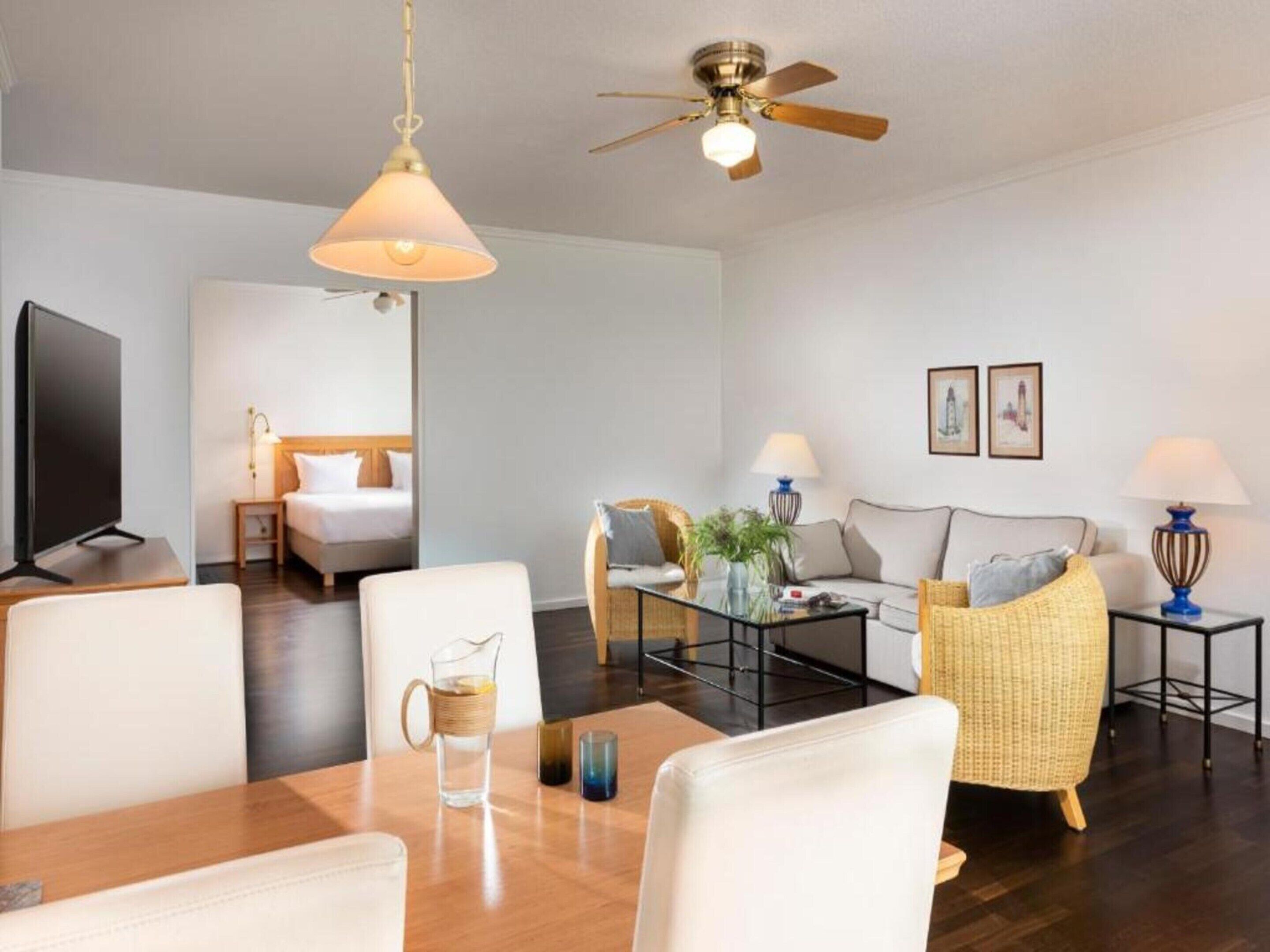 Une chambre d’hôtel moderne dotée d’un coin repas, d’un canapé, d’une télévision et d’un ventilateur de plafond.