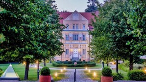 A large, stately building with a symmetrical facade, a central entrance, and a well-maintained garden with a paved pathway leading to the entrance. - Sunday Resort Rugen 2-bedroom Suite (Sagard)