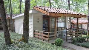 A small, single-story cabin with a porch, surrounded by trees and a garden. - VILLAS HOLIDAYS (Kiten)