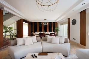 A modern living room with a sectional sofa, a dining area with a round table, and a large window providing natural light.