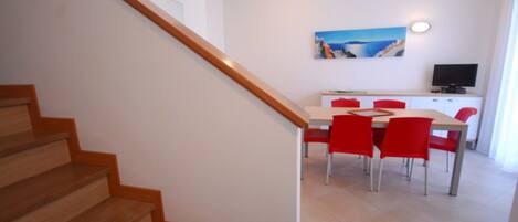 Una escalera conduce a un comedor con una mesa y sillas, un cuadro en la pared y un televisor sobre un mueble.