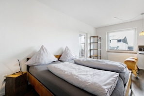 Un dormitorio con dos camas, una ventana, un radiador y una silla de madera.