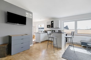 Una cocina moderna con un televisor de pantalla plana, gabinetes grises y suelo de madera.