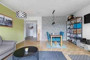 A living room with a sofa, a dining table with chairs, a coffee table, a bookshelf, and a television.