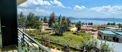 A balcony with a view of a landscaped garden, a body of water, and distant mountains.