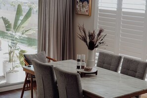 A dining area with a marble table, grey upholstered chairs, a vase with dried plants, and a window with blinds. - A cosy home away from home! (Mandogalup)