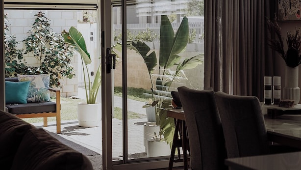 A modern living room with a sliding glass door leading to a balcony with large potted plants.