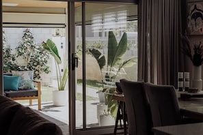 A modern living room with a sliding glass door leading to a balcony with large potted plants. - A cosy home away from home! (Mandogalup)