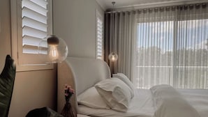 A hotel room with a bed, a round table with a remote control, a vase with flowers, and a lamp.