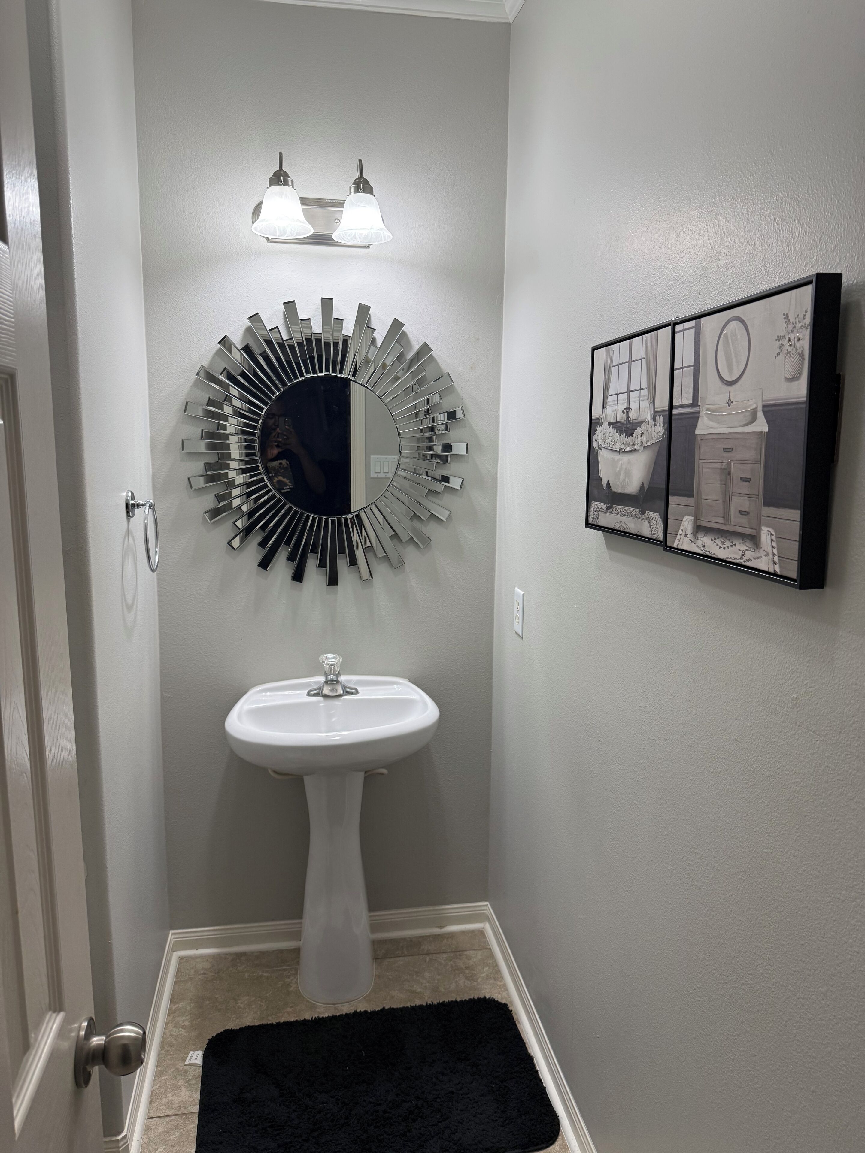 Un baño con un lavamanos pedestal, un espejo montado en la pared y un cuadro con una imagen de baño.