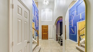 Um corredor com porta de madeira, escada e parede azul com padrões geométricos.