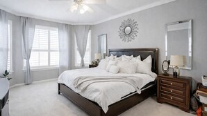 Quarto com uma cama grande, um ventilador de teto, um espelho fixado na parede e uma peça decorativa na parede.