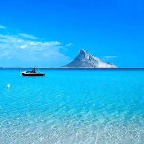 Ein Boot auf klarem türkisblauem Wasser, im Hintergrund ein schneebedeckter Berg.