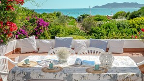 An outdoor dining area with a table set for two, surrounded by white chairs, overlooking a scenic coastal view with greenery and a body of water. - Apartment 'Trilocale Taverna 80m from Beach' with Sea View, Private Terrace & AC (Porto Taverna)