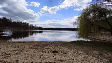 A calm lake with a boat docked on the left, surrounded by trees and a sandy shore.