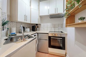 A compact kitchen with white cabinets, a stainless steel sink, a dishwasher, and an oven. - Stylish 2 bed - Tower Hamlets (Greater London)