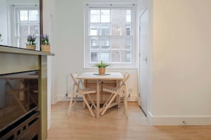A room with a wooden table and chairs, a window with a view of buildings, and a door. - Stylish 2 bed - Tower Hamlets (Greater London)