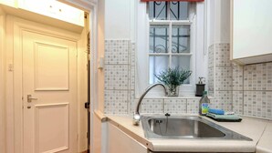 A kitchen with a sink, a window with a plant, and a door. - Stylish 2 bed - Tower Hamlets (Greater London)