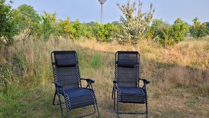 To sorte stole med metalstel, mesh-ryg og -sæde, placeret på en græsplæne med en stenkø ved siden af.
