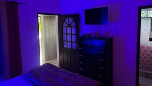 A bedroom with a bed, a dresser, a television, and a door leading to another room. - 1-bedroom apartment in marvelous Ocho Rios with AC comfort (Ocho Rios)