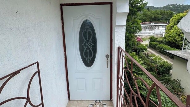 A white door with a decorative glass panel and a metal gate on a balcony with patterned tiles. - 1-bedroom apartment in marvelous Ocho Rios with AC comfort (Ocho Rios)