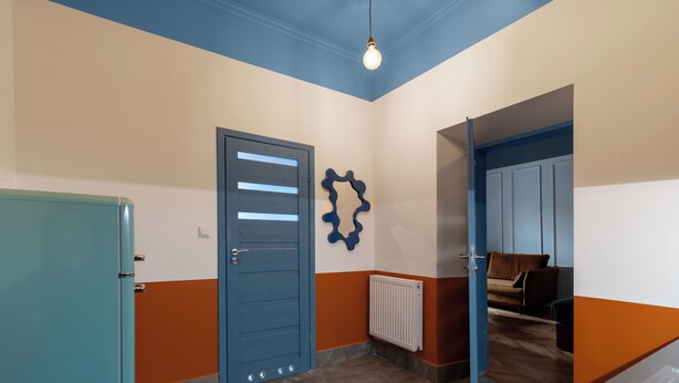 Ein Zimmer mit blauer Tür, Heizkörper und braunem Sofa.