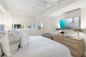 Un dormitorio con cama, mesita de noche, lámpara, cómoda y un amplio ventanal con persianas.