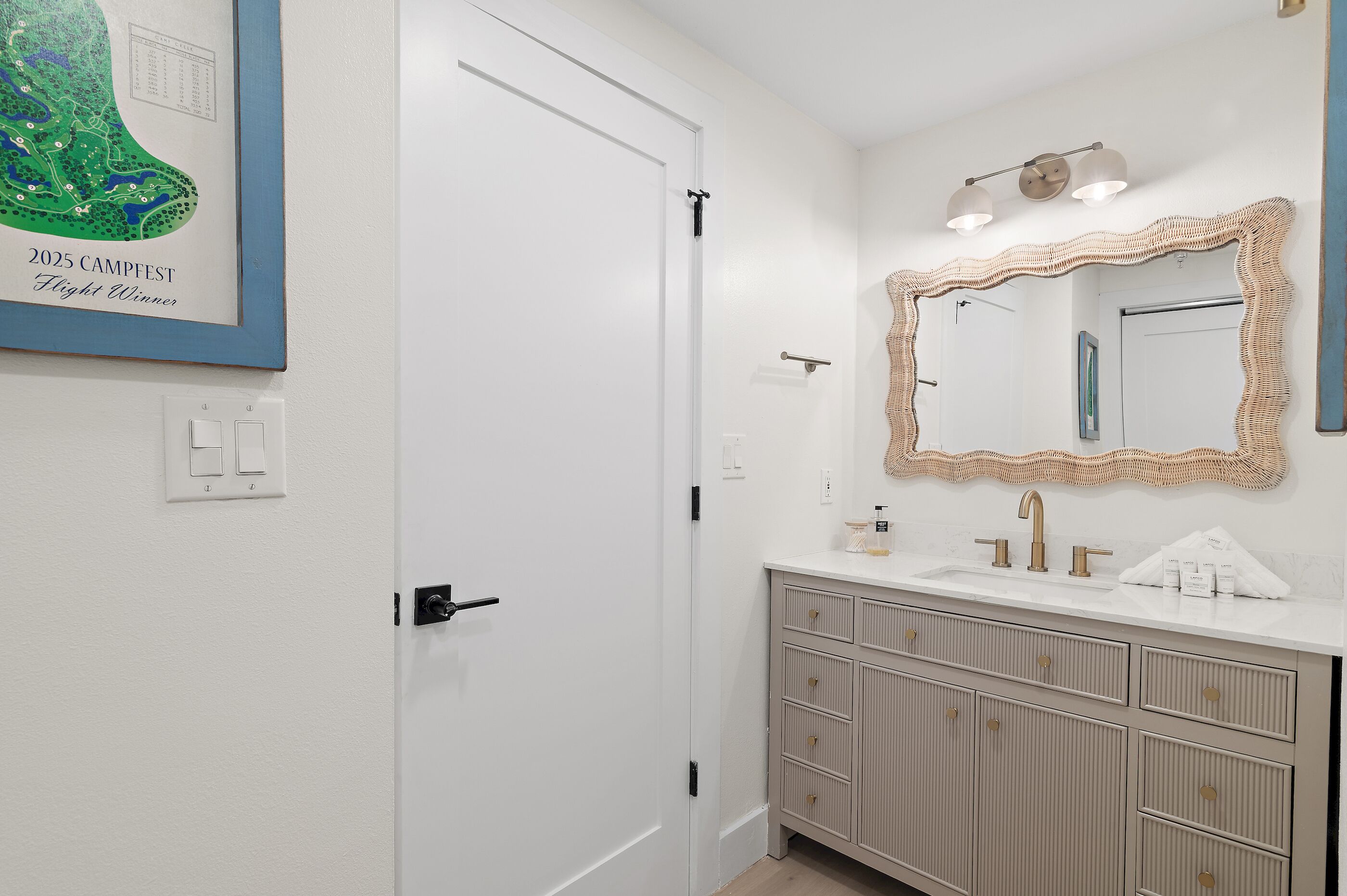 Une salle de bain avec une porte blanche, un lavabo avec un miroir et une carte encadrée accrochée au mur.