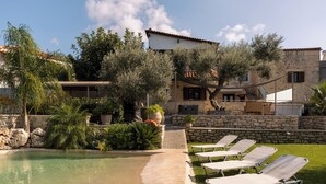 A pool area with lounge chairs, a stone wall, and a building with a tiled roof. - Countryside Villa with a Walk-in Free Form Pool (Rethymno)