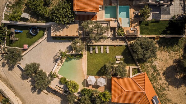 Luchtbeeld van een resort met meerdere zwembaden, een tennisbaan en een verzorgd gazon.