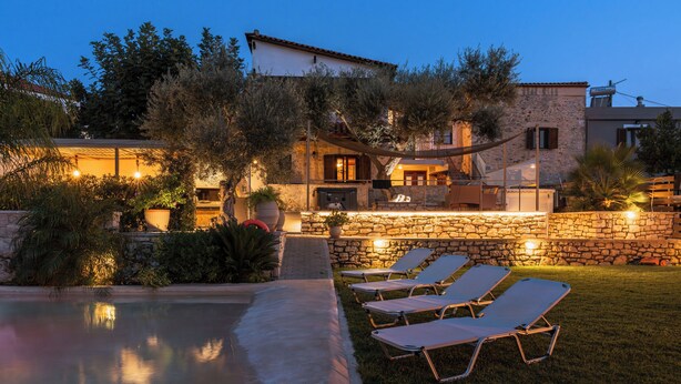 A poolside area with lounge chairs and a stone wall. - Countryside Villa with a Walk-in Free Form Pool (Rethymno)